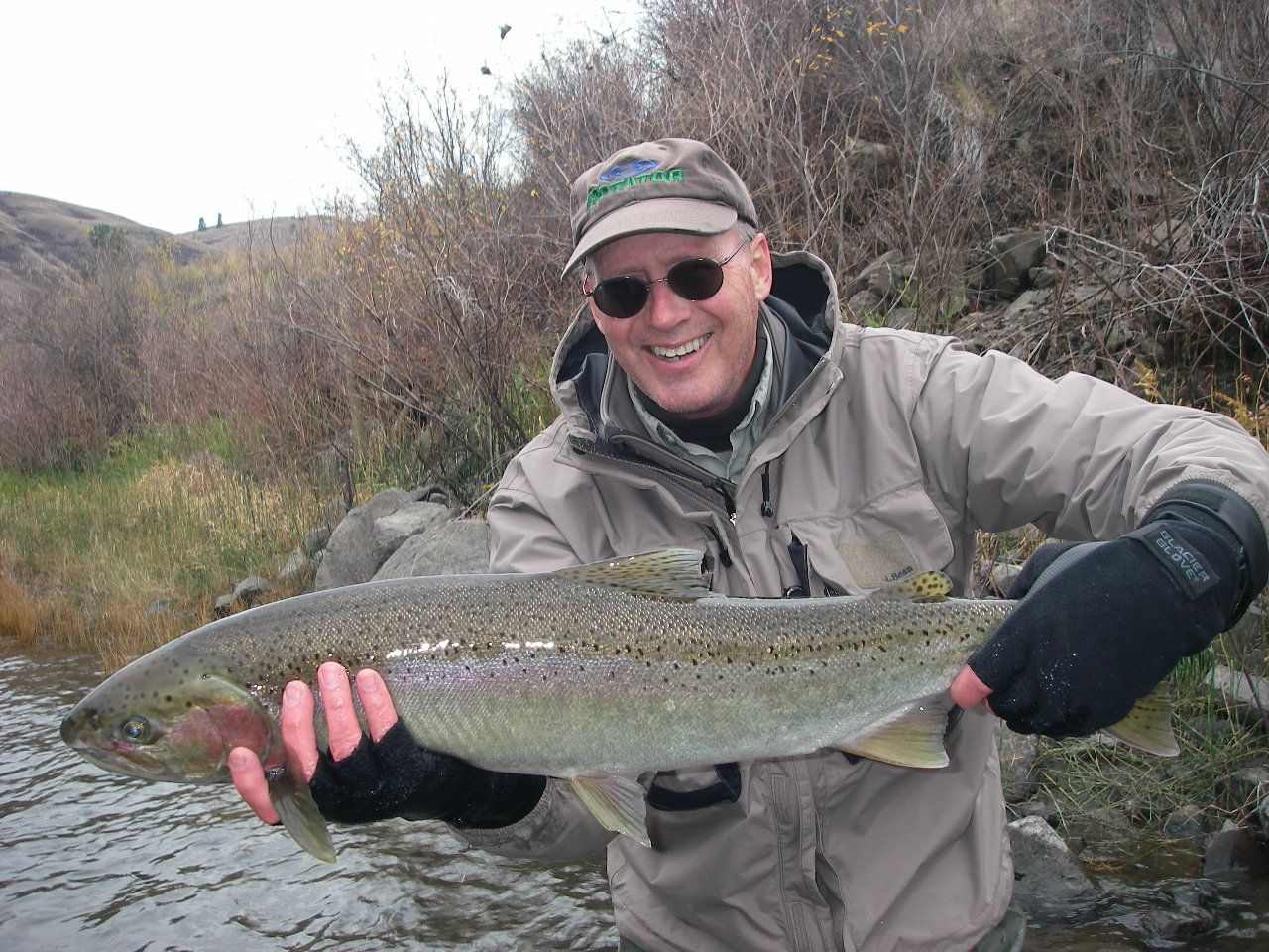 A man is holding a large fish in his hands in front of a river.