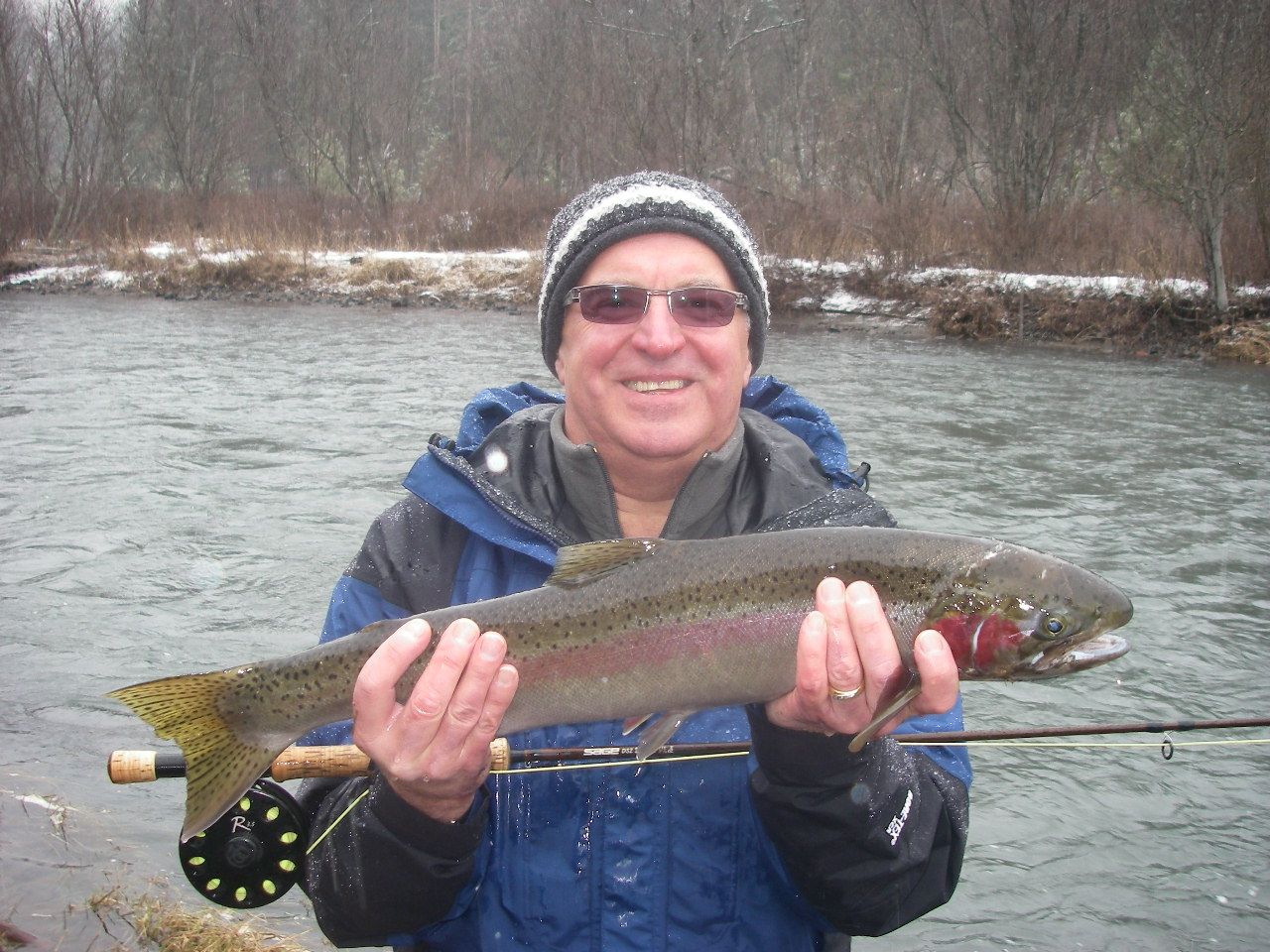 A man in a blue jacket is holding a rainbow trout