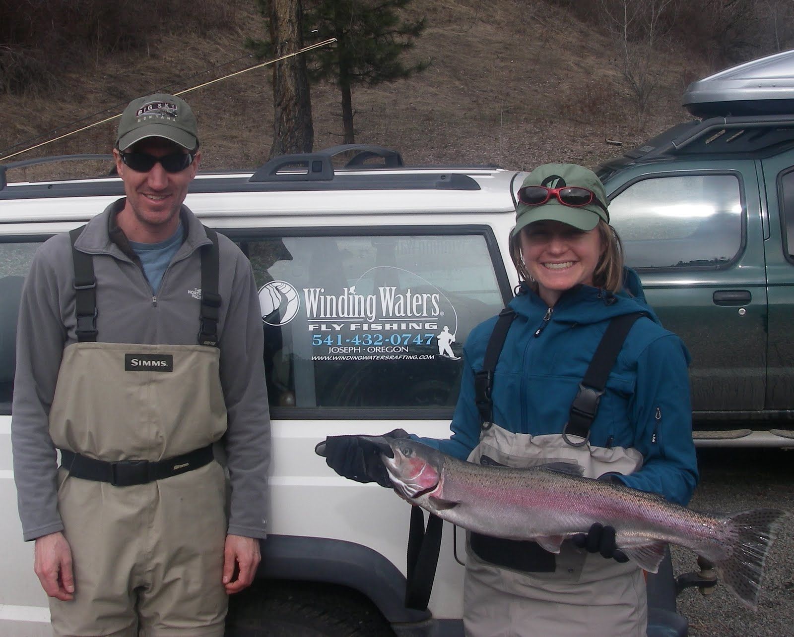 A man and a woman holding a fish in front of a vehicle that says wildflow masters