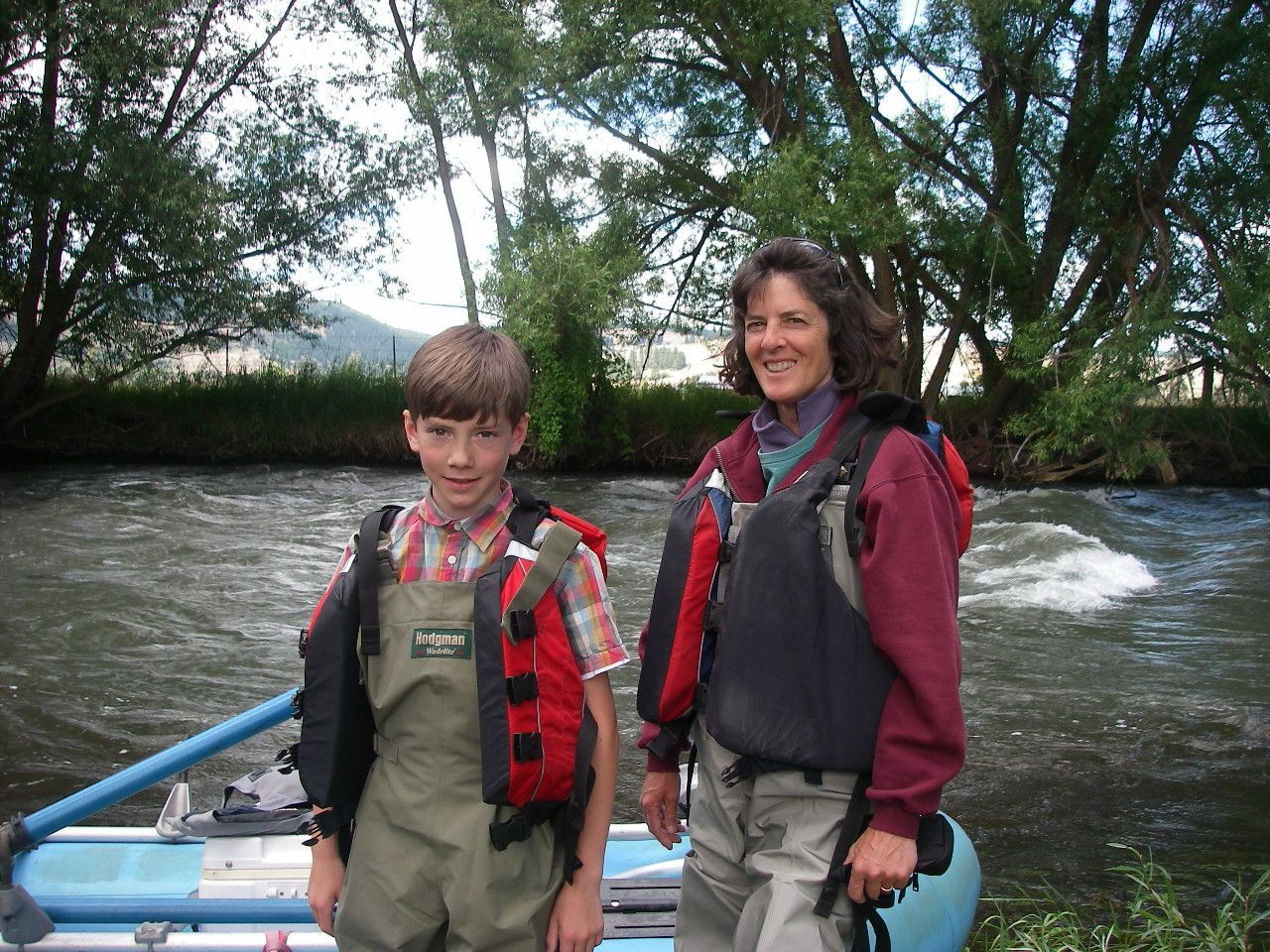 A woman and a boy are standing next to a raft in a river