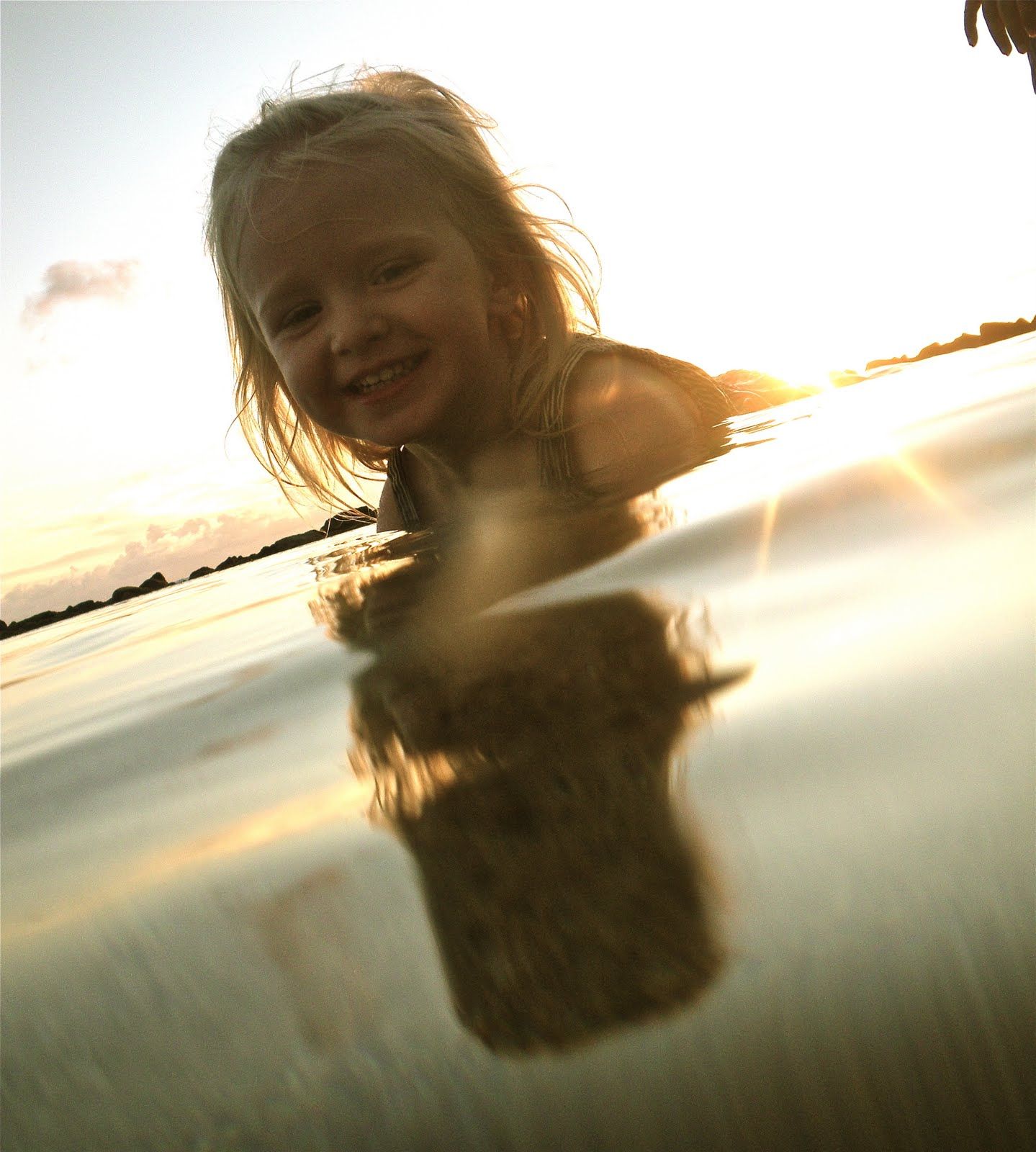A little girl is swimming in the water and her reflection is in the water