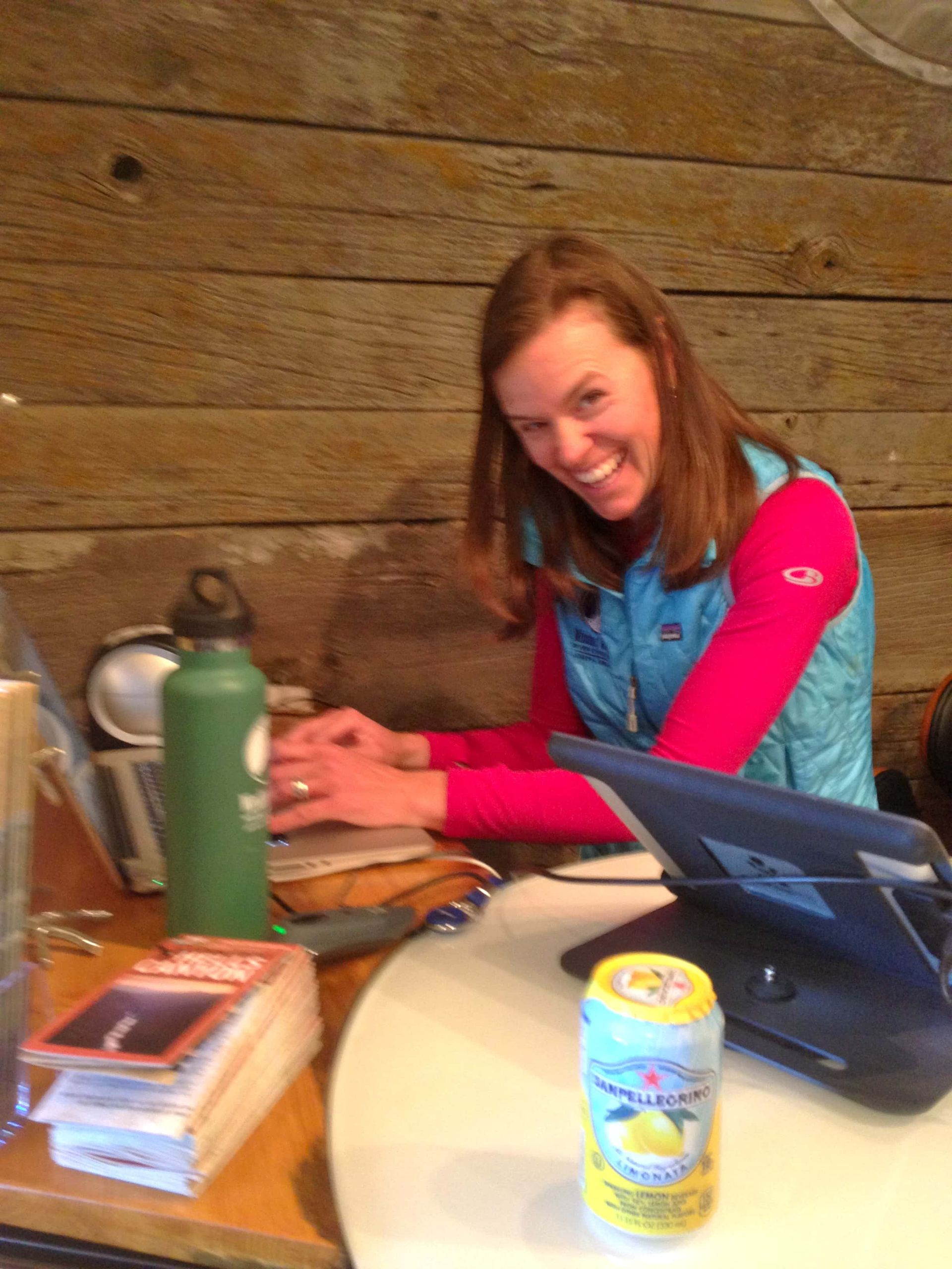 A woman sits at a table with a laptop and a can of lemonade