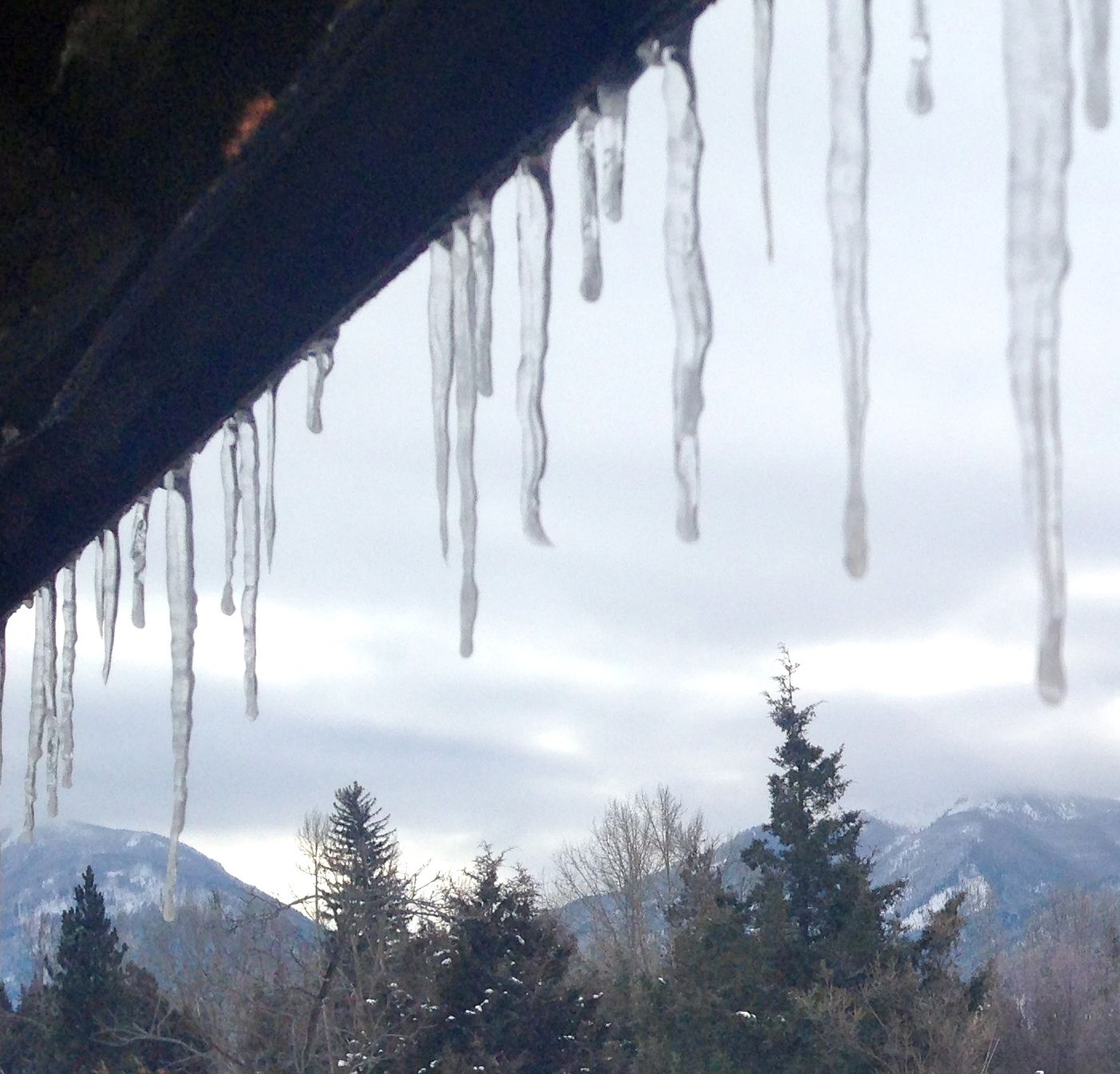 Icicles hanging from a roof with mountains in the background