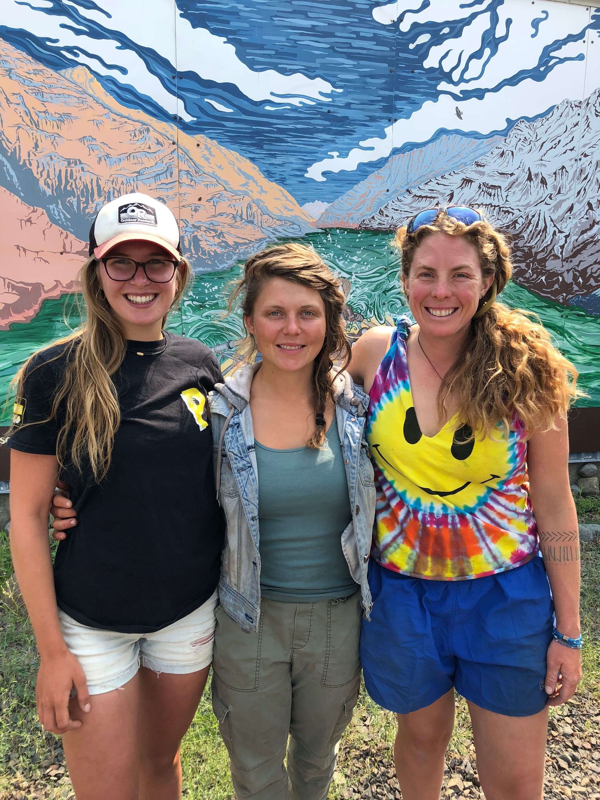Three Women Posing for A Picture in Front of A Mural