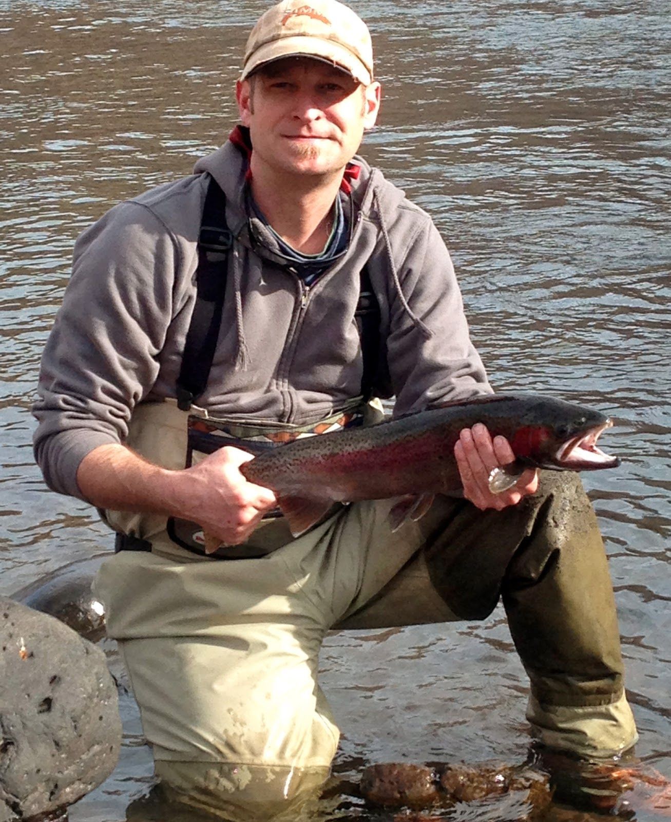A man is kneeling in the water holding a large fish