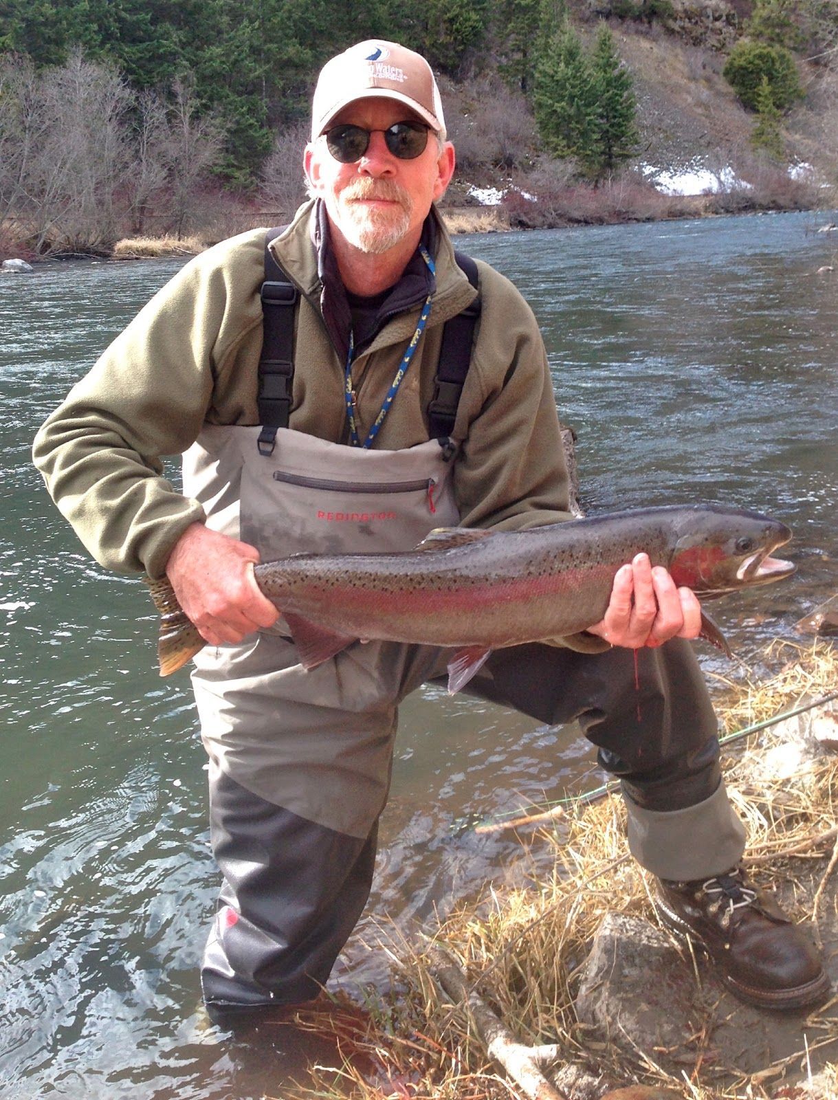 A man is kneeling in the water holding a large fish