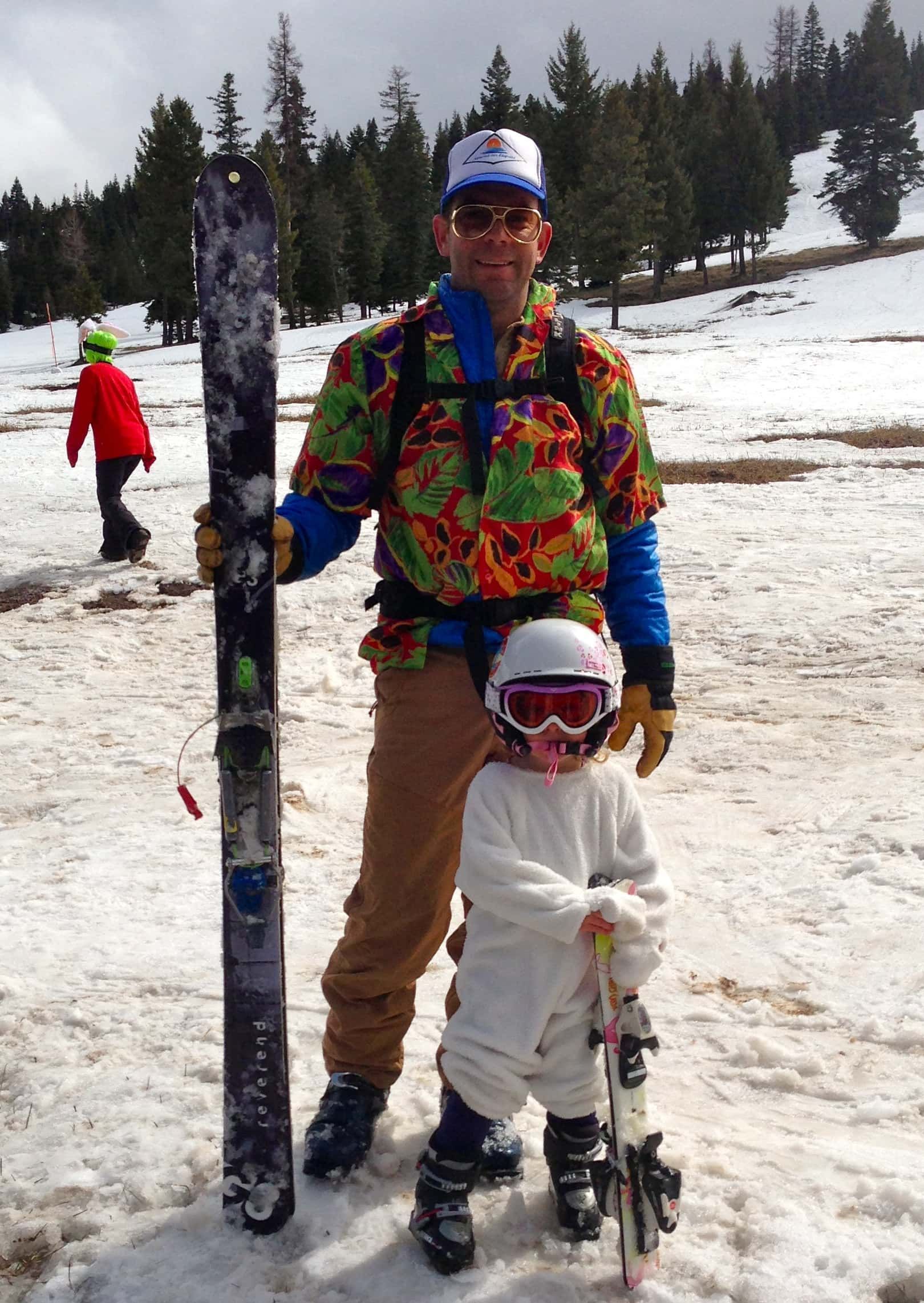 A man and a child are standing in the snow holding skis