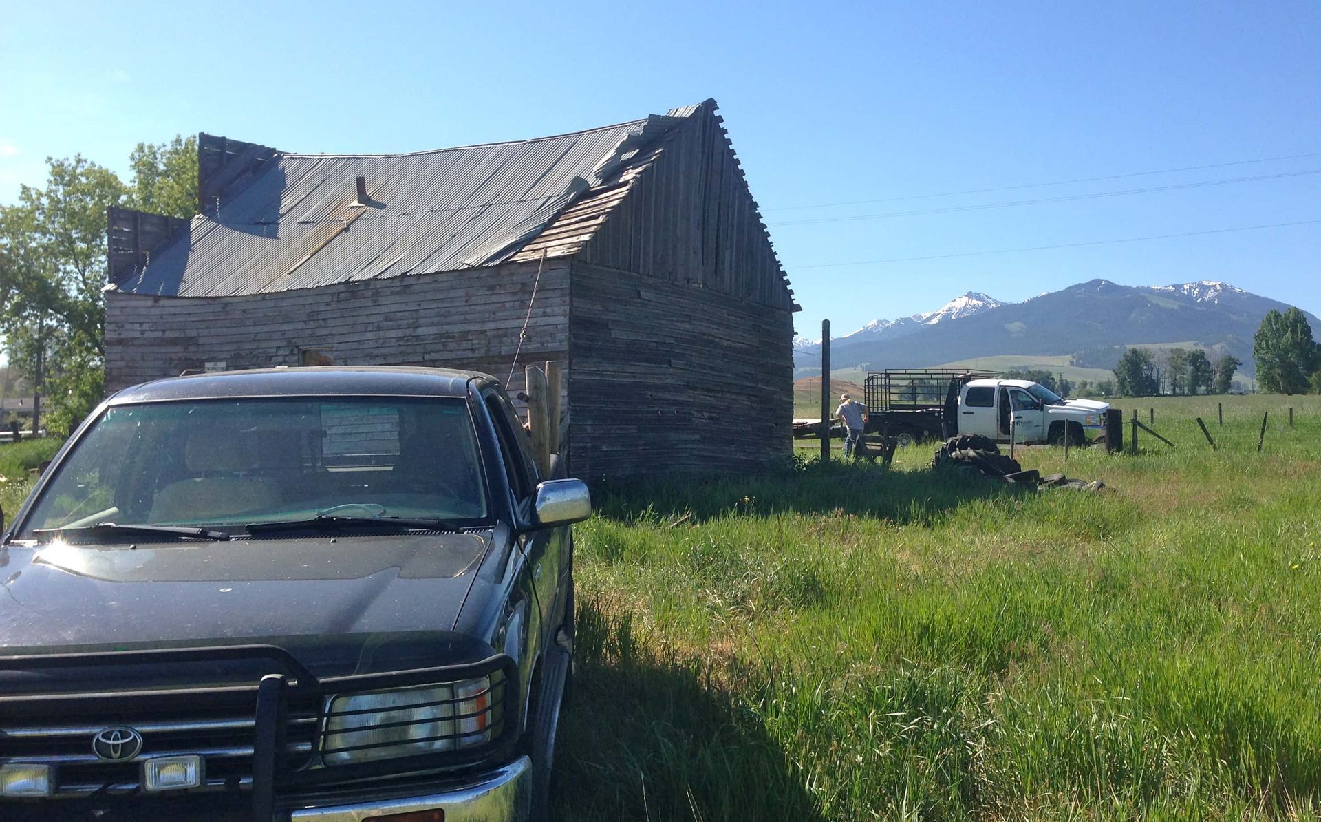 A truck is parked in a grassy field in front of an old barn.