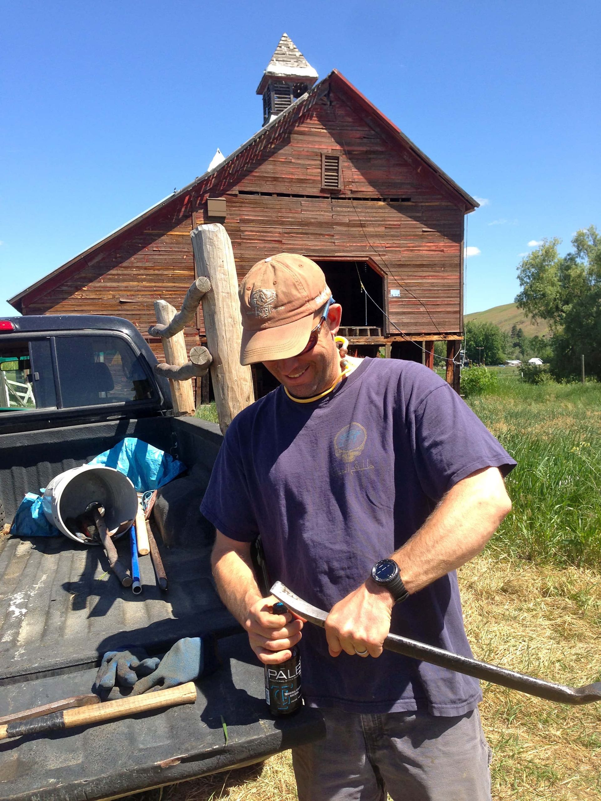 A man is standing in front of a barn holding a shovel.