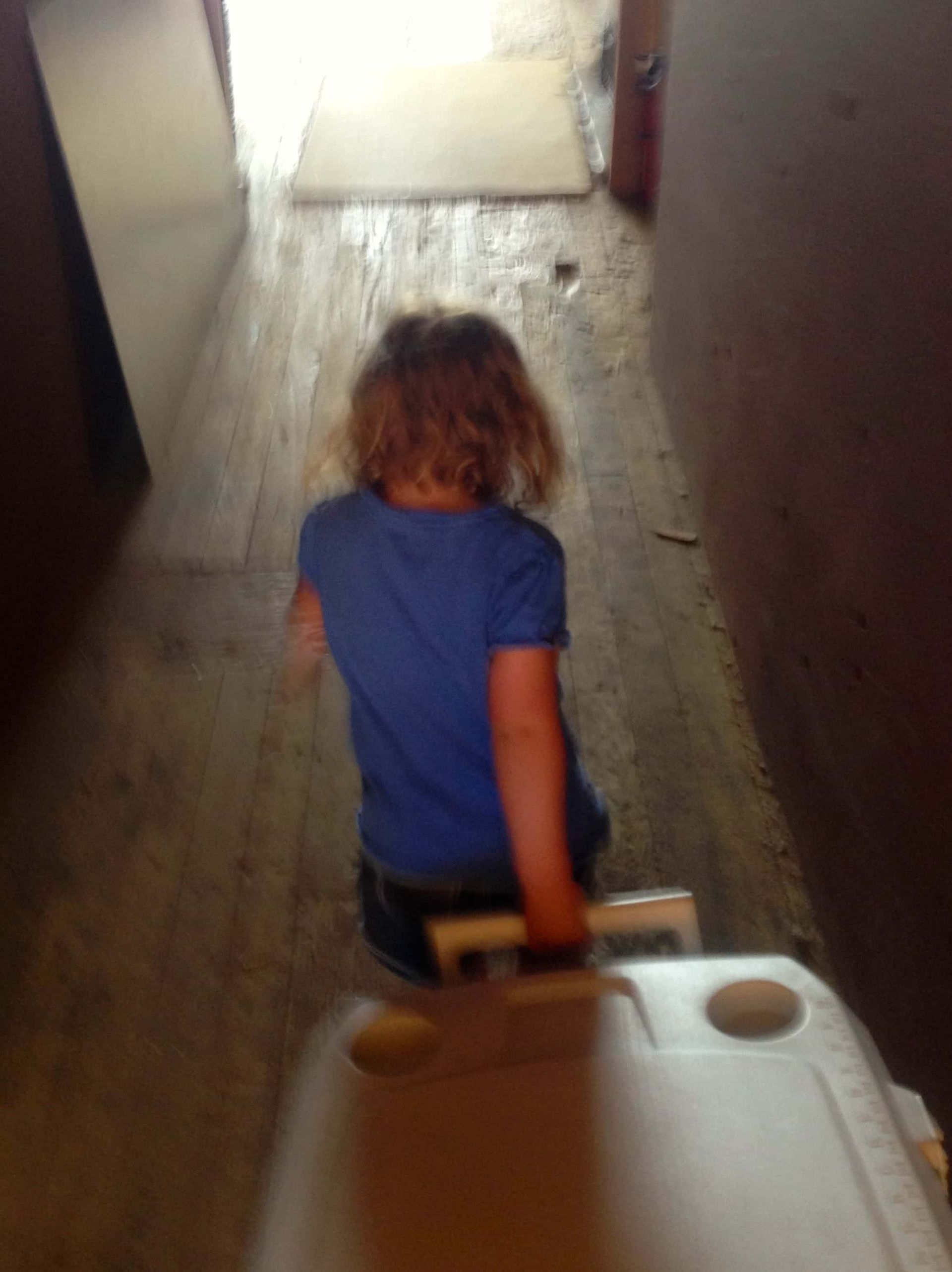 A little girl is pushing a cooler down a hallway.