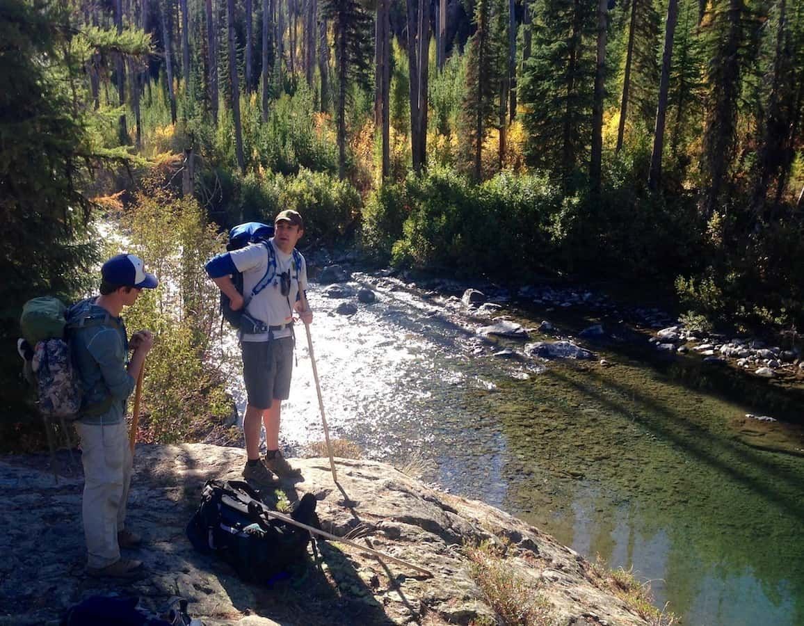 Two people are standing next to a river in the woods.