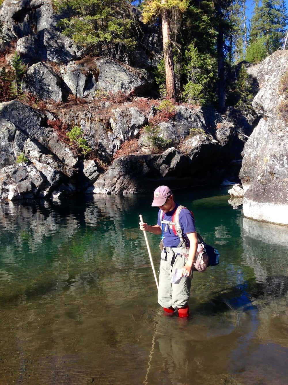 A man is standing in the water holding a stick.