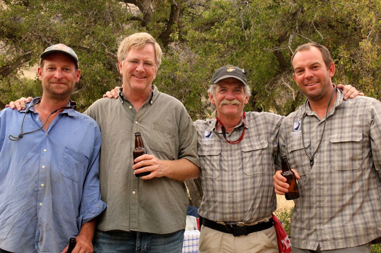 Four men posing for a picture with one holding a bottle of beer
