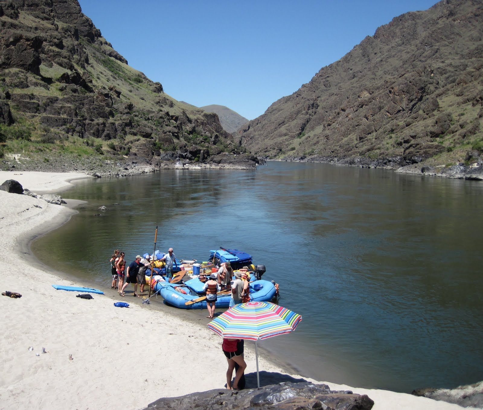 A group of people are standing on a beach near a river