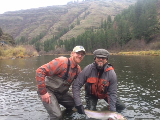 Two men are kneeling in a river holding a large fish