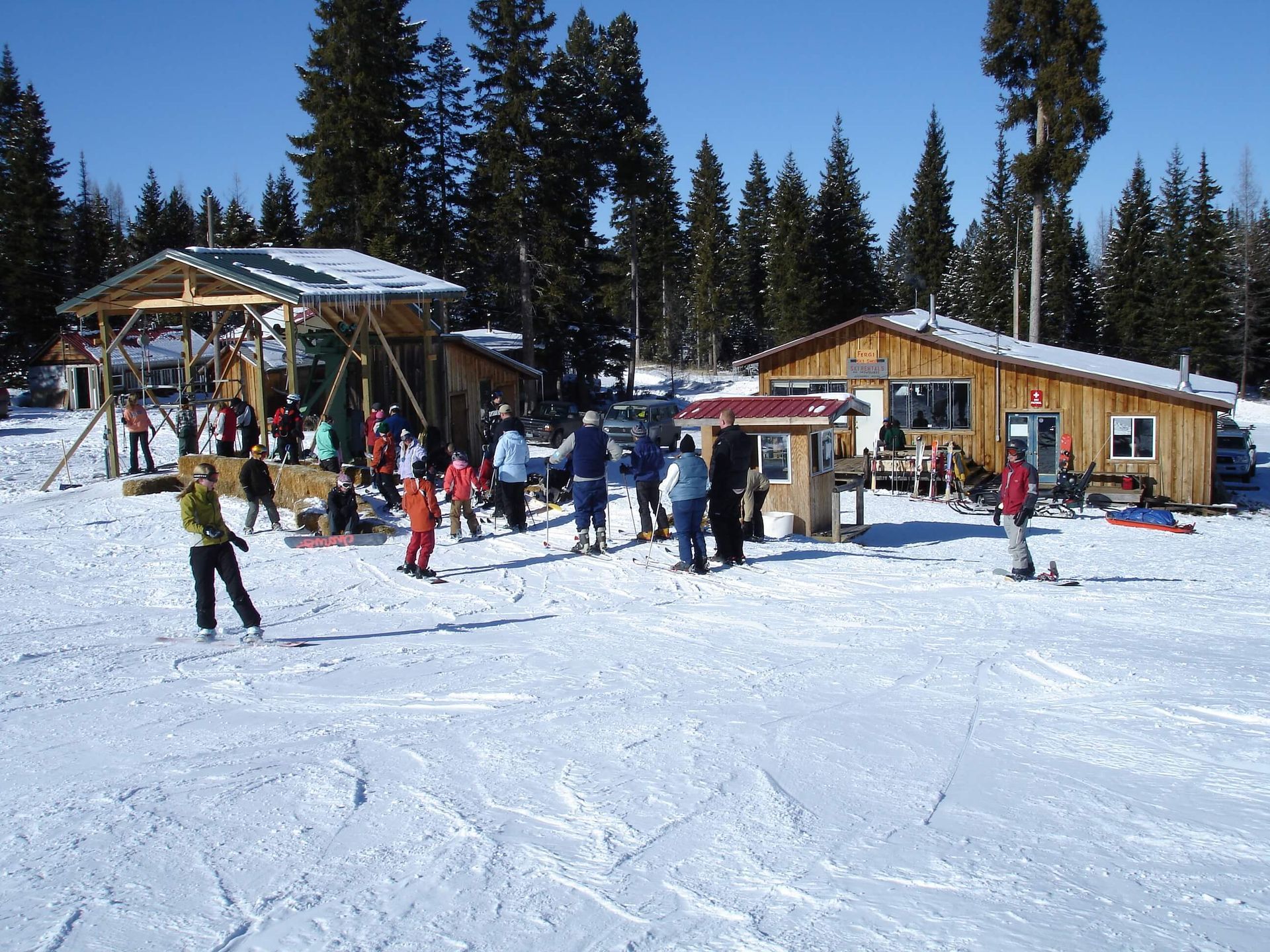 A group of people are standing in the snow near a wooden building