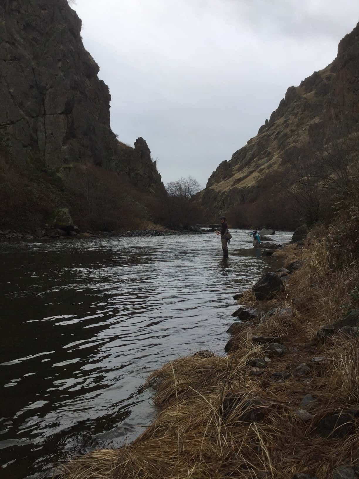 A man is fishing in a river surrounded by mountains