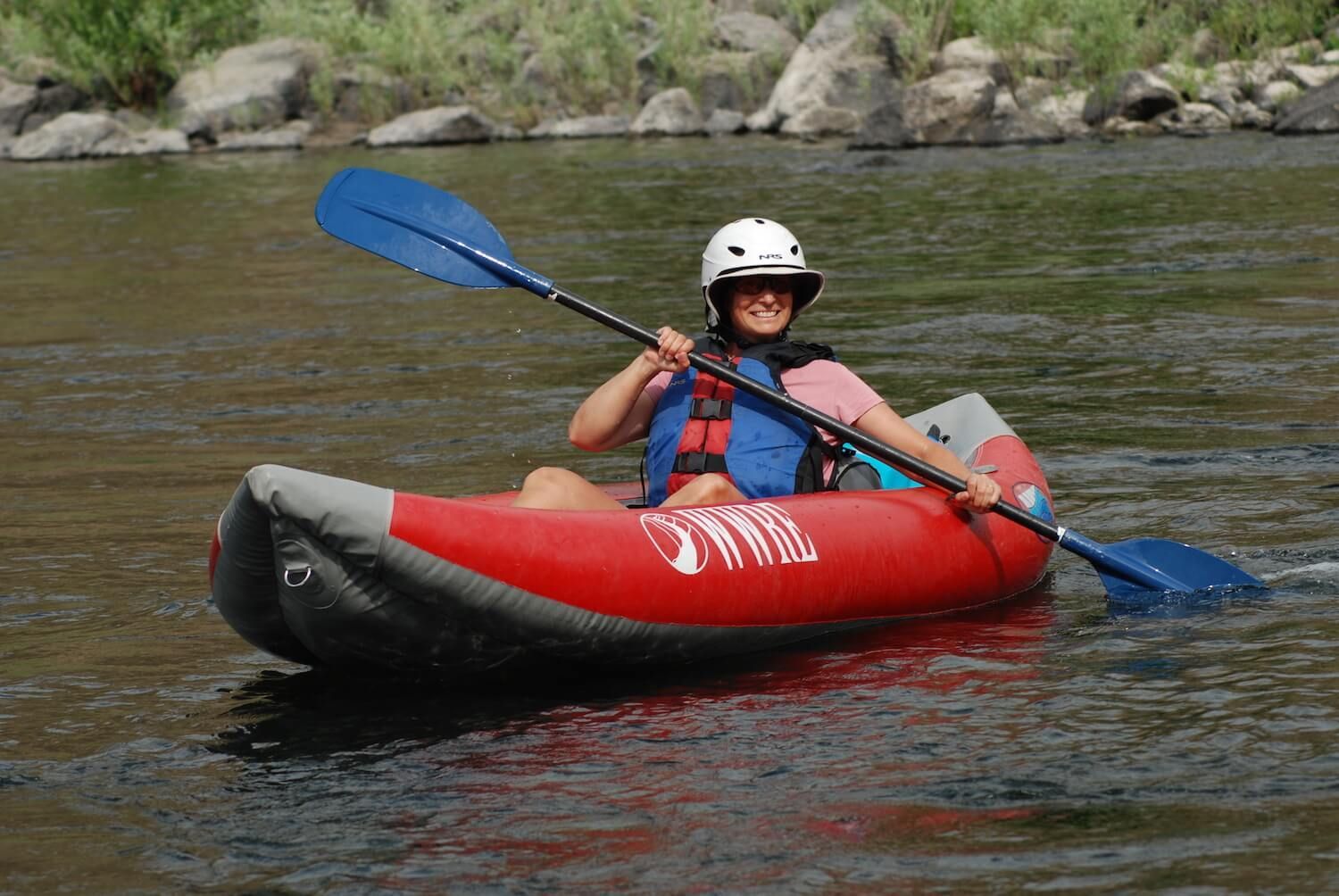 A woman is paddling a red kayak on a river.
