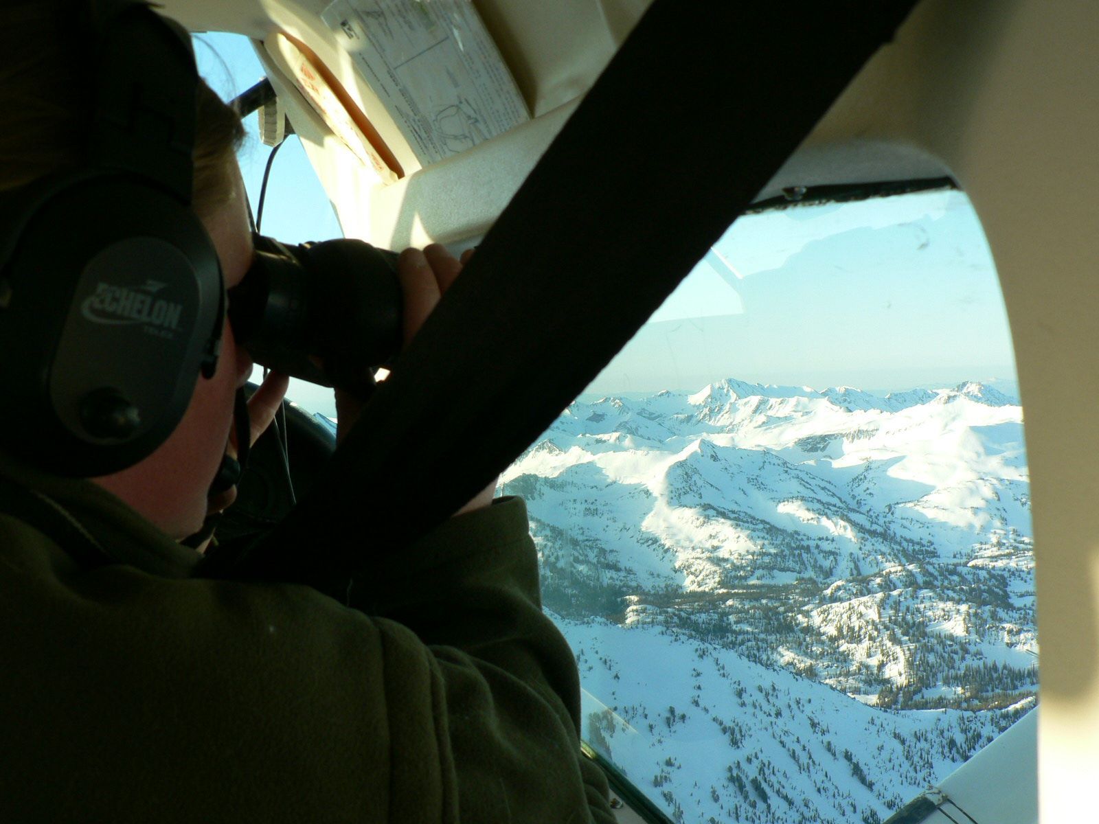 A man wearing headphones looks out the window of an airplane