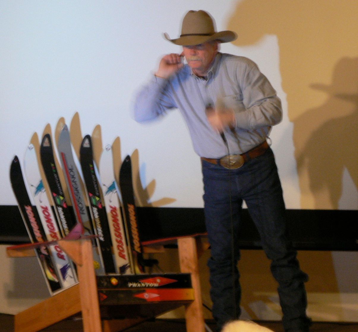A man in a cowboy hat stands in front of a row of skis that say rossignol