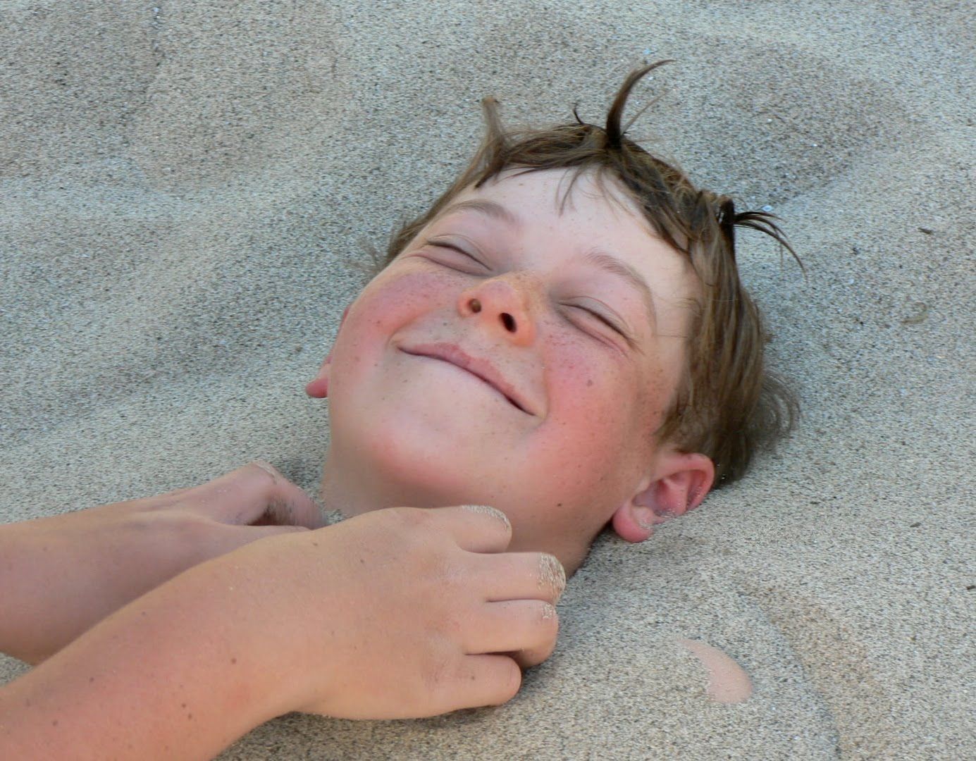 A young boy is laying in the sand and smiling.