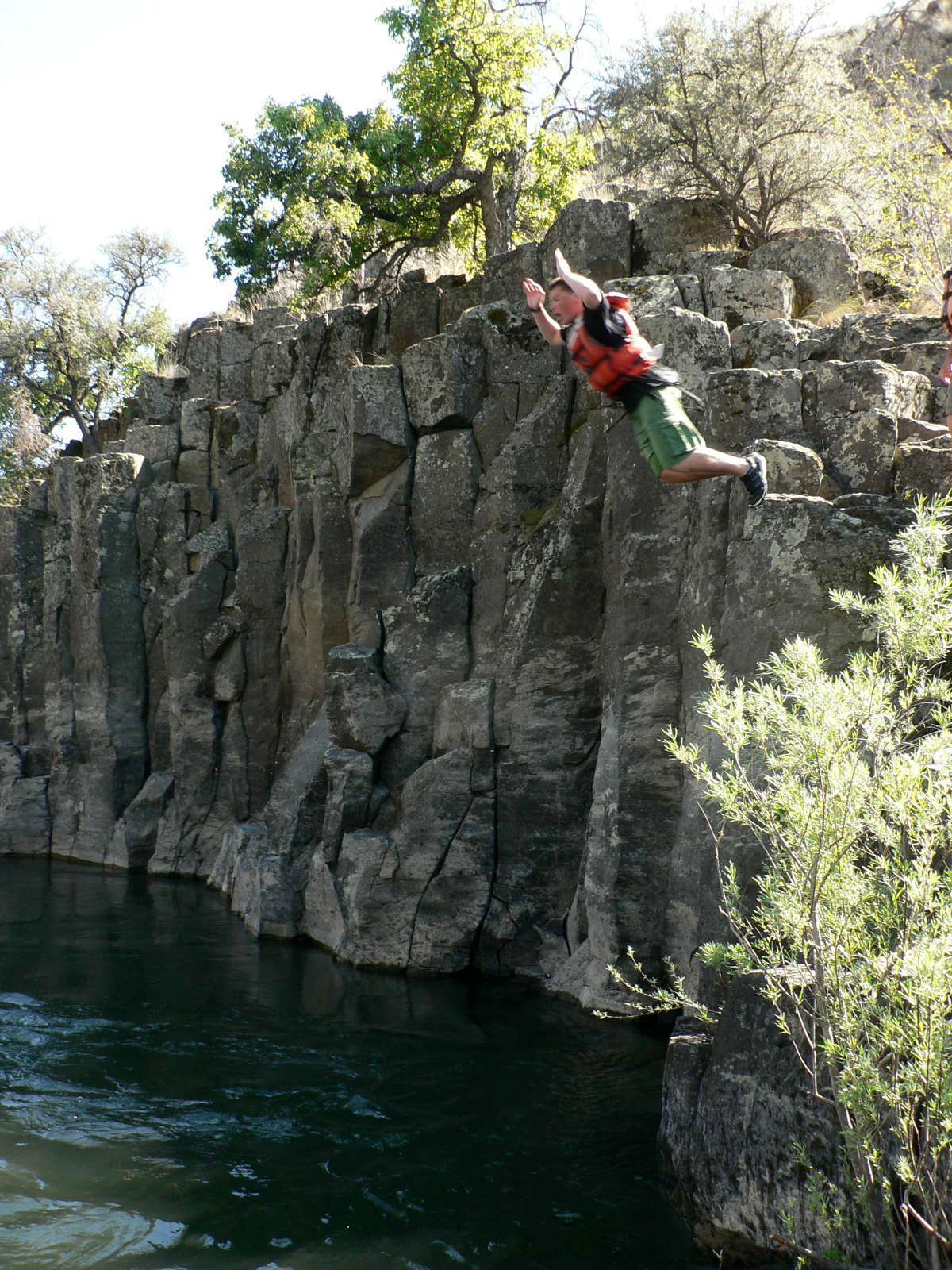 A man is jumping off a cliff into a body of water