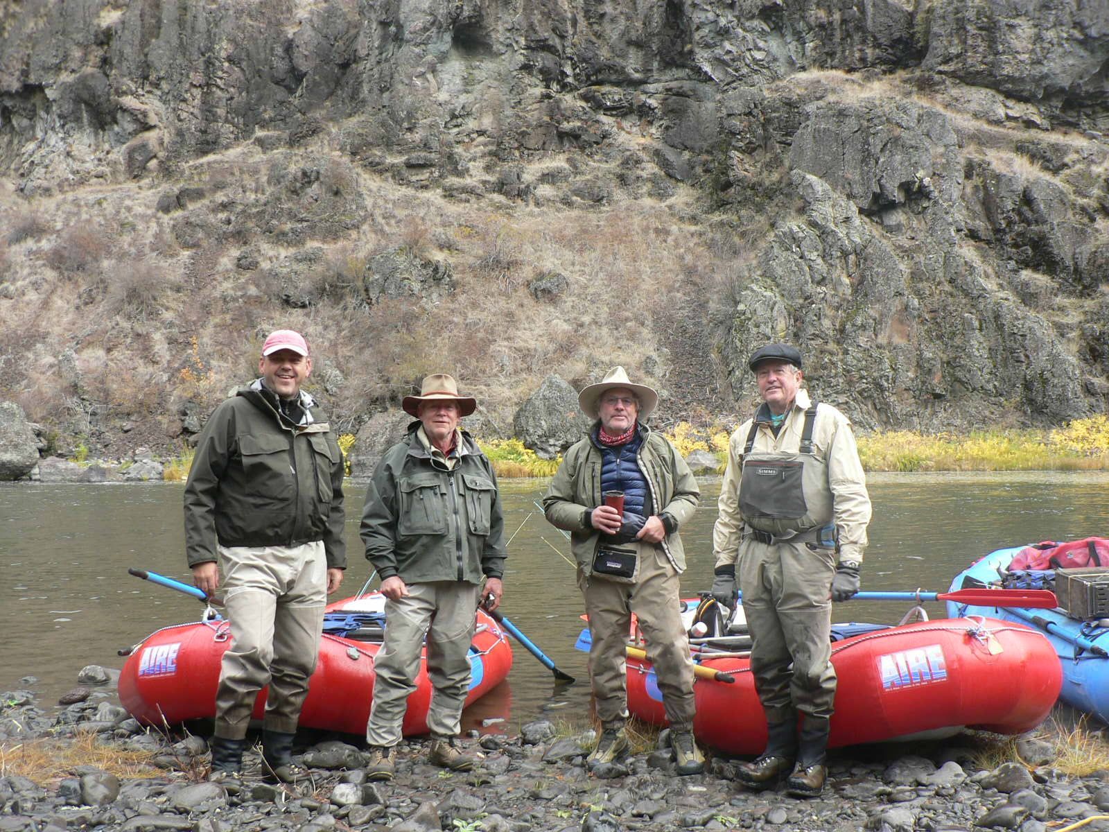 A group of men are standing next to rafts on the shore of a river.