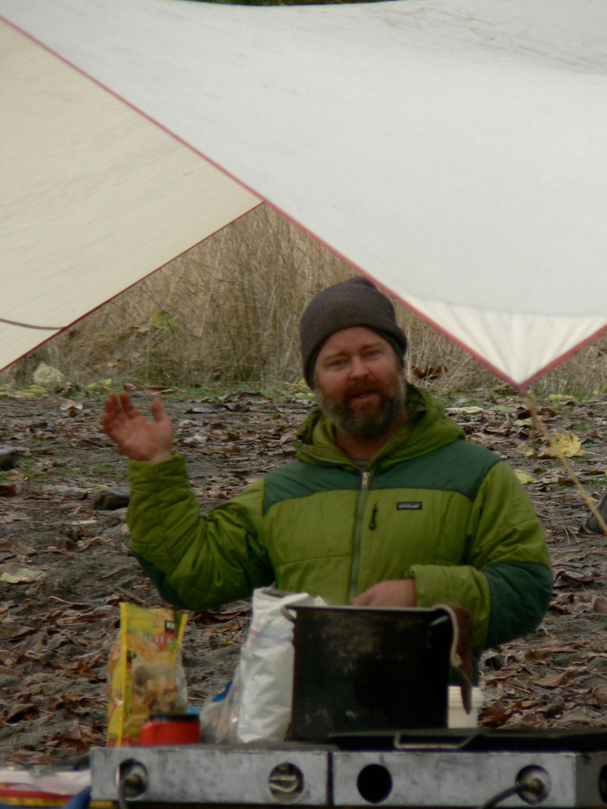 A man in a green jacket is standing under a white tarp