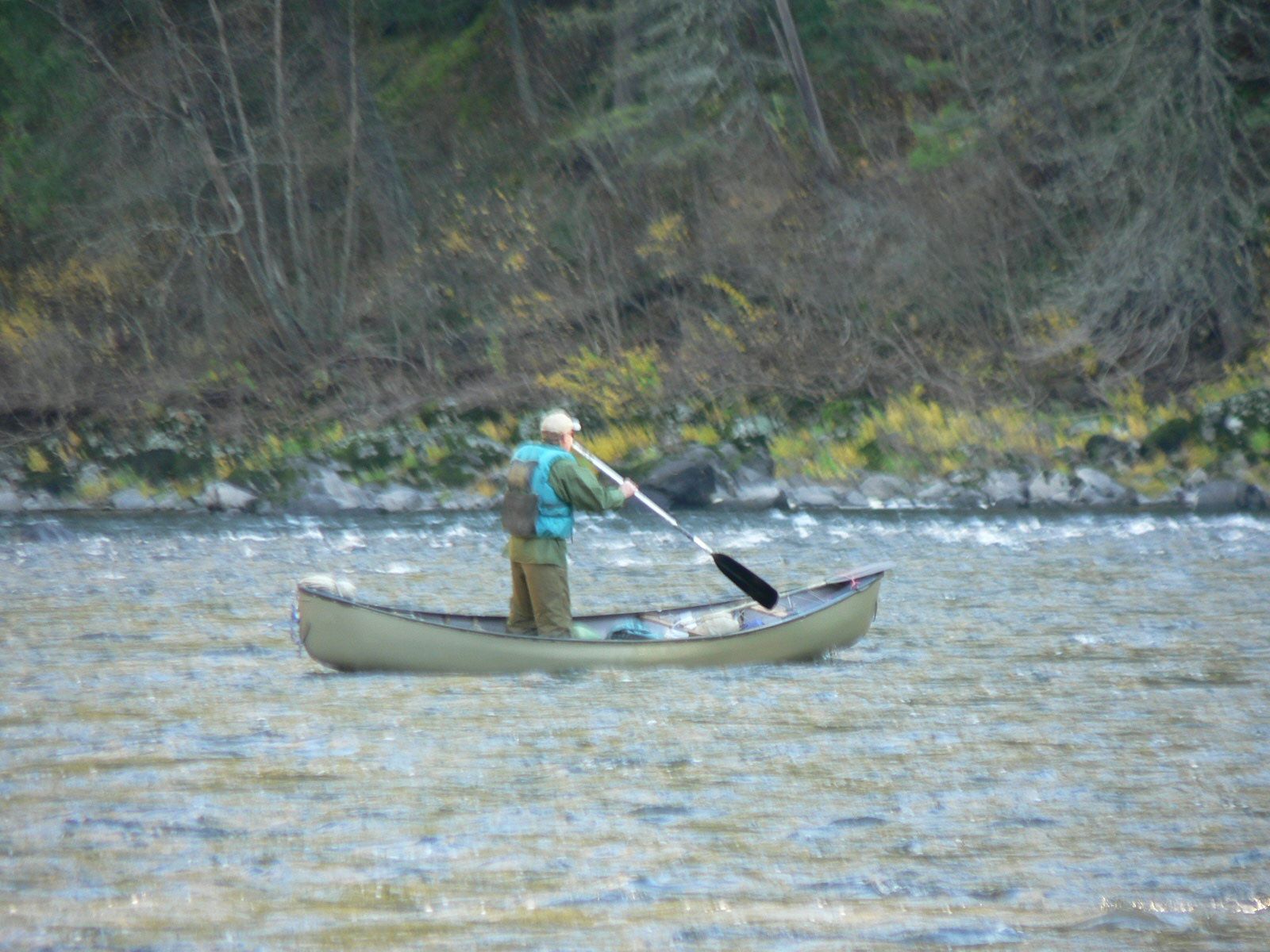 A man is rowing a canoe down a river.