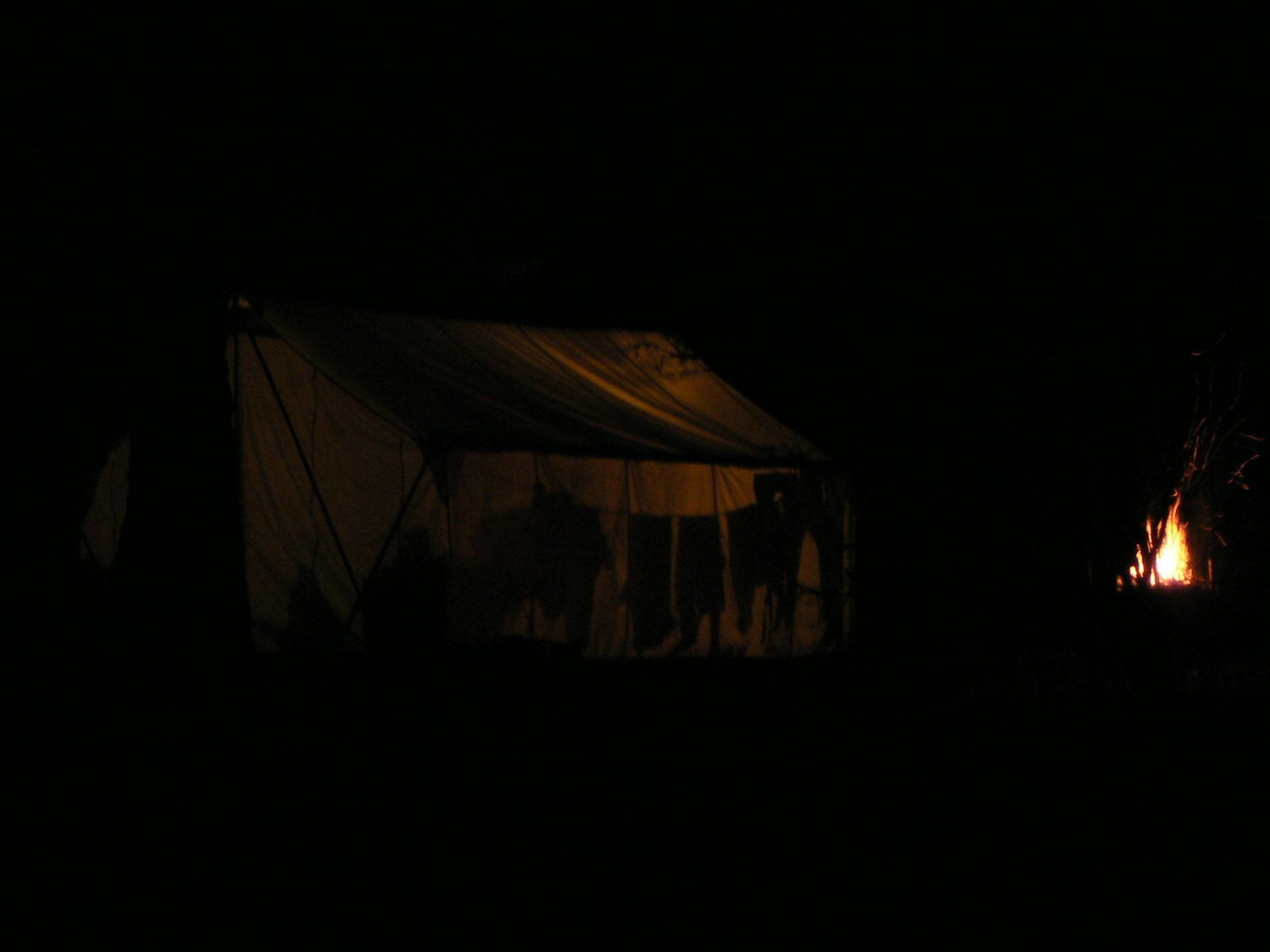 A tent is lit up at night with a fire in the background.