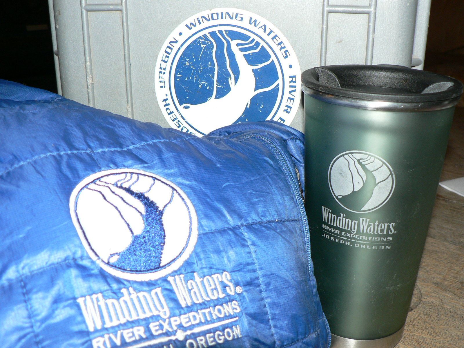 A blue winding waters river expeditions blanket sits next to a green cup