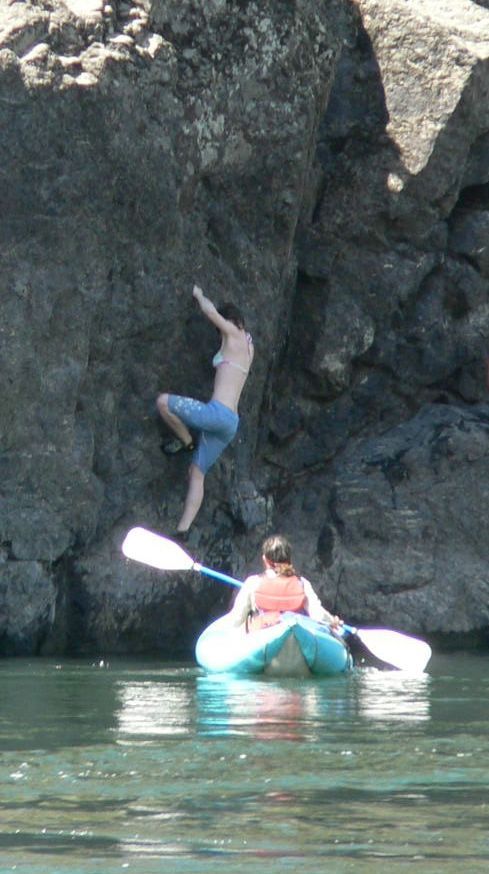 A man is climbing a rock while a woman is in a kayak.