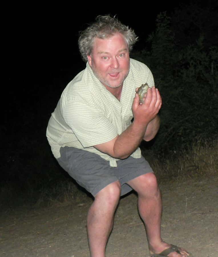 A man squatting down holding a frog in his hands
