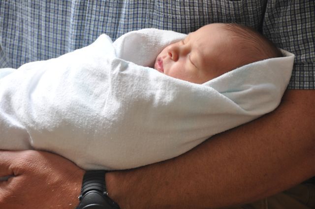 A man is holding a newborn baby wrapped in a white blanket.
