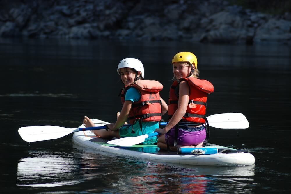 Two Young Girls Are Riding a Paddle Board in The Water 
