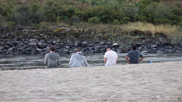 Three Men Are Sitting on the Beach Near a River