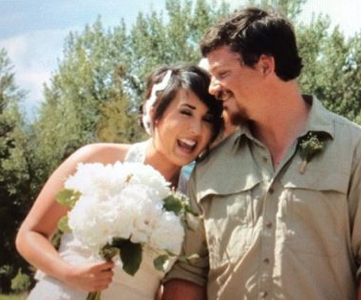 A bride and groom are posing for a picture and the bride is holding a bouquet of white flowers