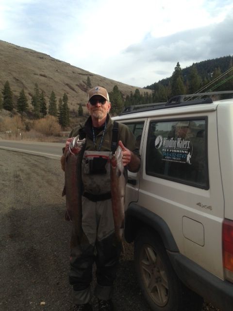 A man is holding two fish in front of a white jeep