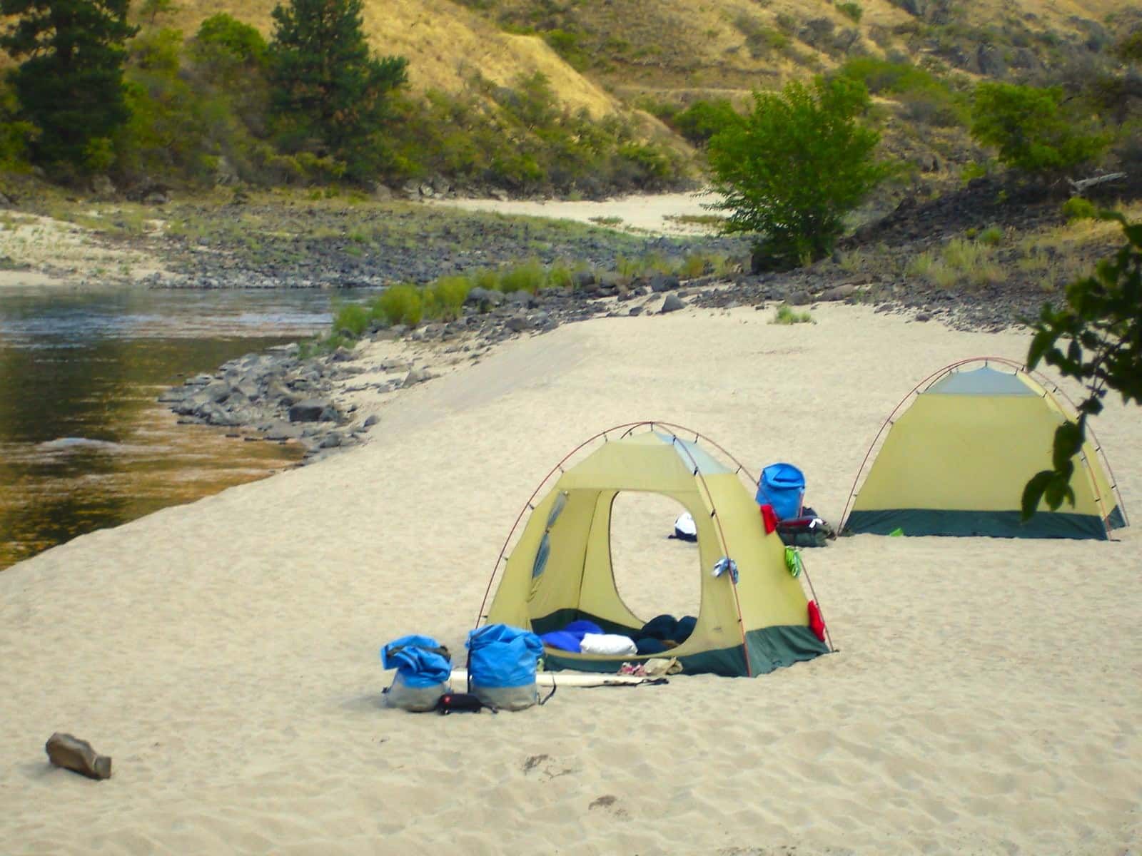 Three Tents Are Set up On a Sandy Beach Near a River