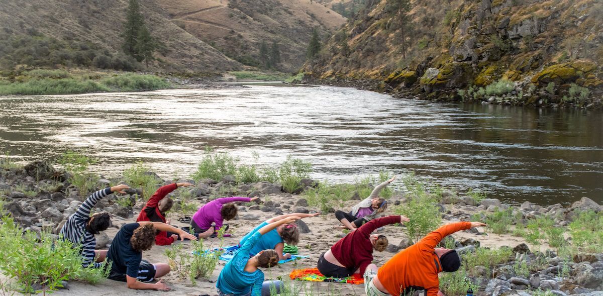 A group of people are doing yoga on the shore of a river.