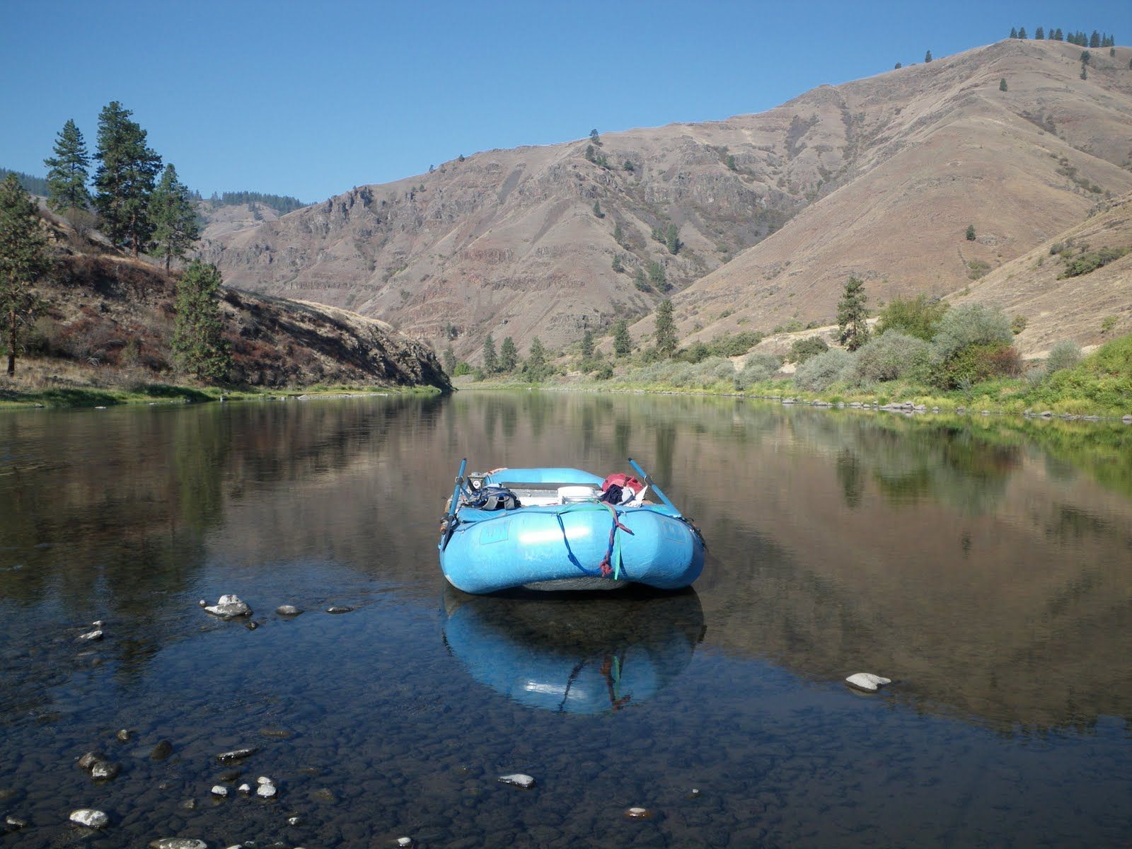 A blue raft is floating on a river with mountains in the background