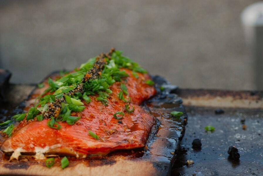 A piece of salmon with green onions on a wooden cutting board.