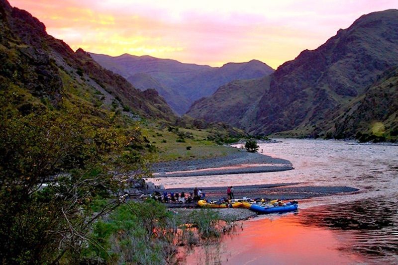 Group of People Are Rafting Down a River with Mountains in The Background
