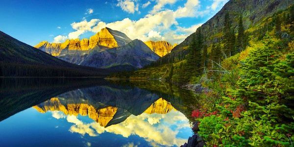 A lake surrounded by mountains and trees with mountains reflected in the water.