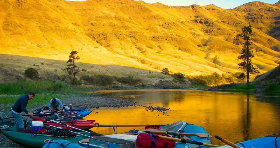 A group of rafts are sitting on the shore of a river with mountains in the background.