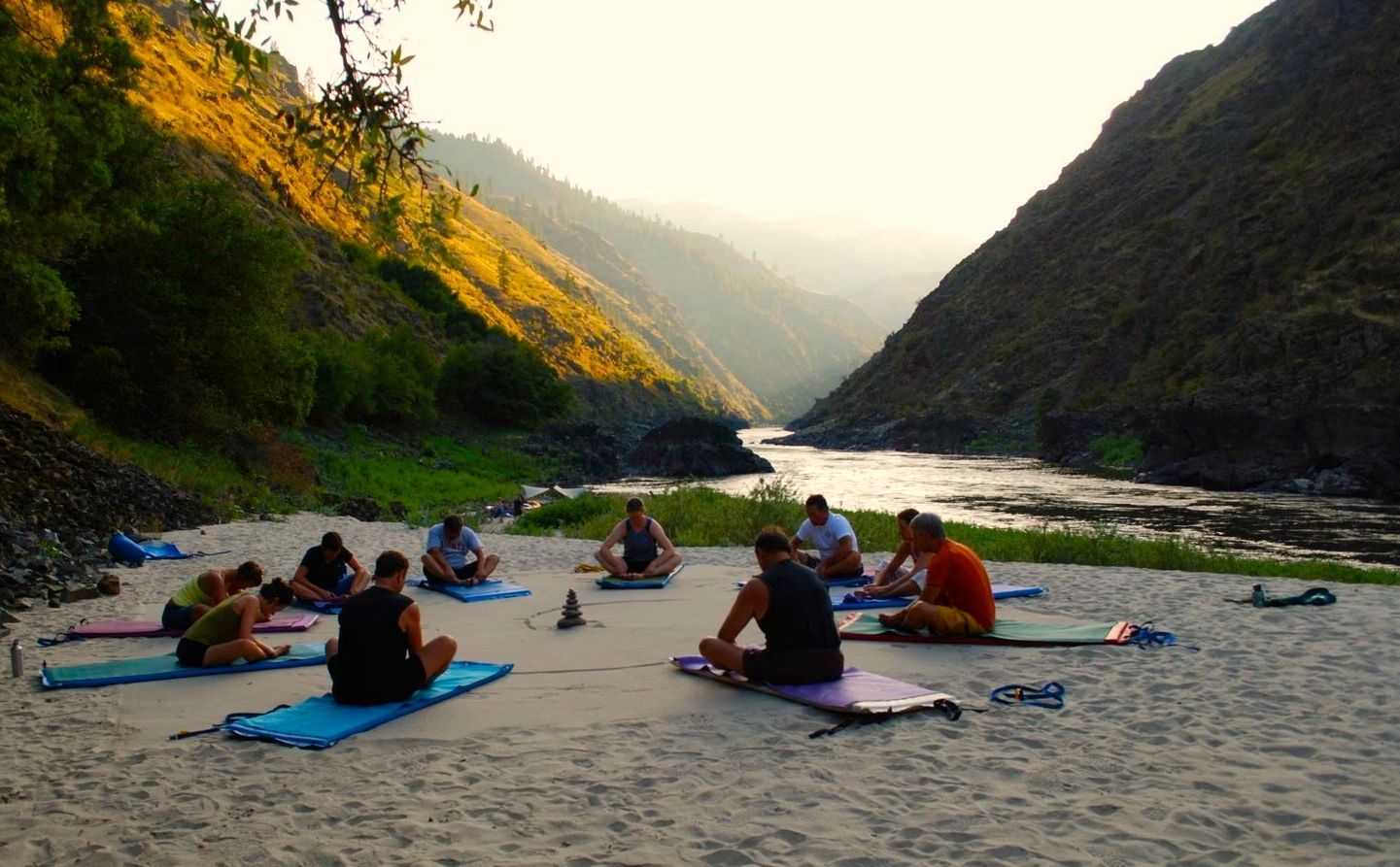 A group of people are sitting on yoga mats near a river