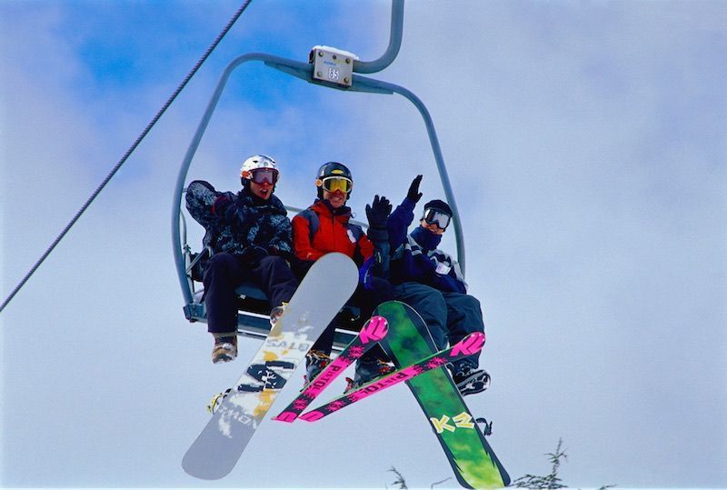 A group of people riding a ski lift with snowboards and skis