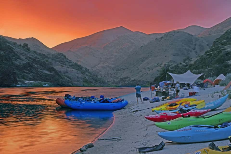 A row of kayaks are lined up on the beach next to a river.