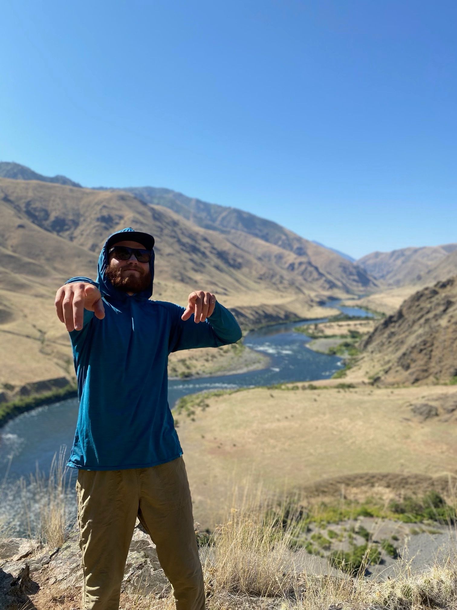 A Man Is Standing on Top of A Hill Pointing at The Camera
