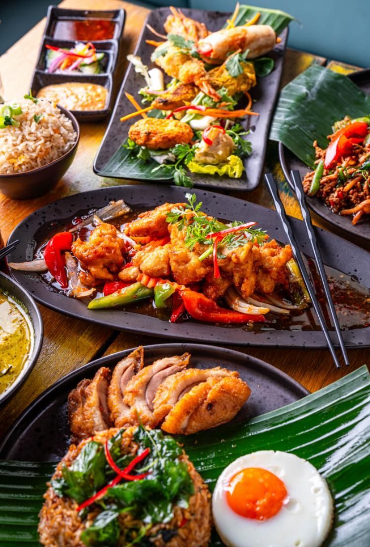 Assorted colorful Japanese dishes on black plates, including grilled meat, sushi, rice, and eggs on banana leaves